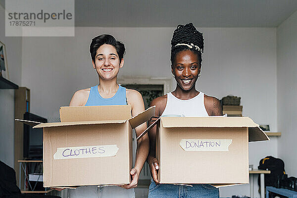 Glückliches lesbisches Paar trägt Kisten für Kleiderspenden zu Hause