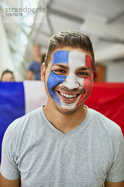 Lächelnder Mann mit französischer Flagge im Gesicht im Stadion