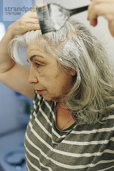 Ältere Frau trägt zu Hause Farbstoff mit Haarbürste auf