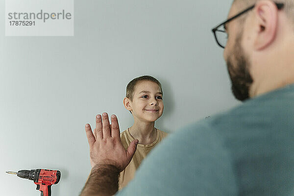 Lächelnder Junge gibt seinem Vater vor der Wand High-Five
