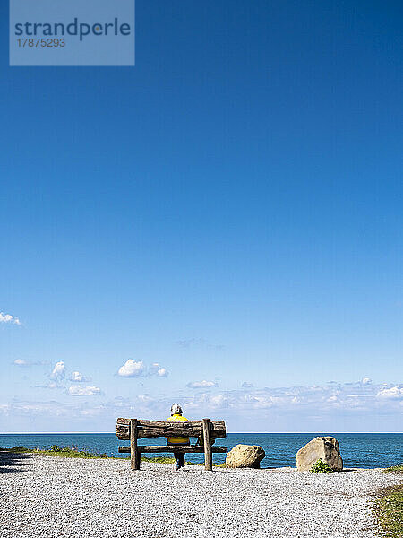 Frau sitzt auf einer Bank am Meer
