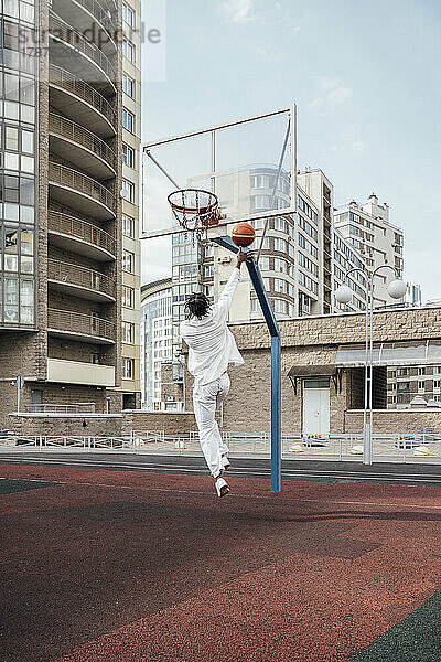 Junger Mann wirft Basketball auf Sportplatz