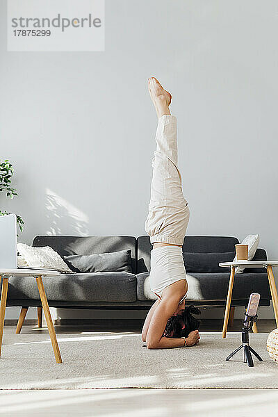 Frau macht Kopfstand im Online-Yoga-Kurs zu Hause