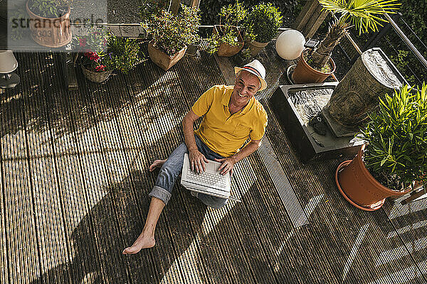 Glücklicher Mann mit Laptop auf der Terrasse sitzend