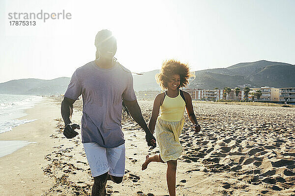 Vater und Tochter laufen Händchen haltend am Strand