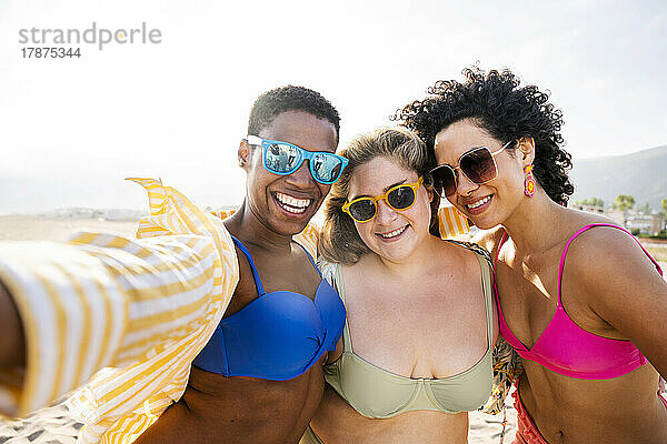 Gemischtrassige Freunde mit Sonnenbrille machen Selfie am Strand