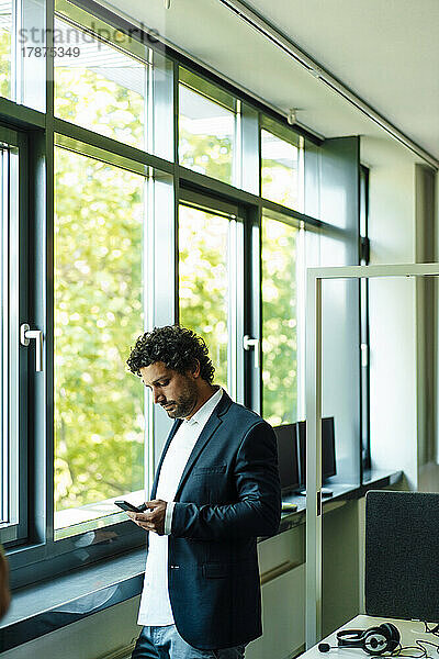 Geschäftsmann benutzt Mobiltelefon am Fenster im Büro