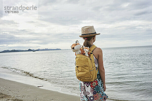 Mädchen mit Stofftieren in der Tasche und Blick aufs Meer