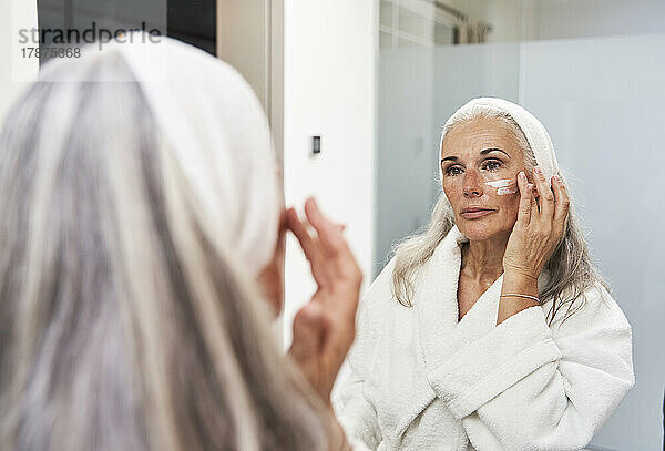 Reife Frau trägt Gesichtscreme im Badezimmer auf
