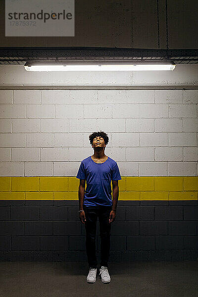 Man with eyes closed standing in illuminated underground walkway