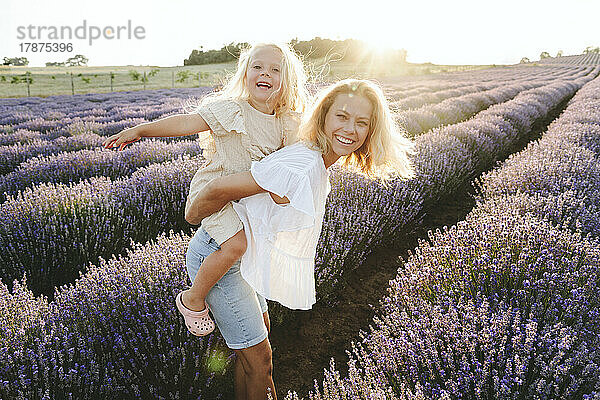 Glückliches Mädchen genießt Huckepack-Fahrt auf Mutter im Lavendelfeld