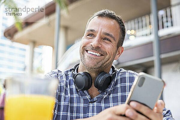 Glücklicher reifer Mann mit Smartphone und kabellosen Kopfhörern im Café