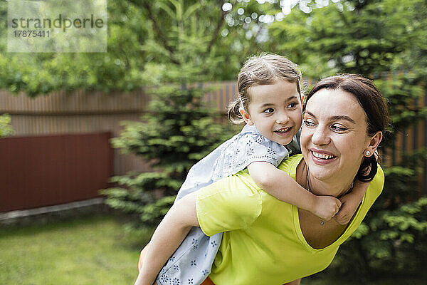 Lächelnde Mutter gibt ihrer Tochter eine Rucksackfahrt im Hinterhof