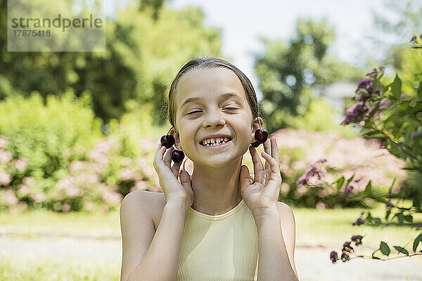 Lächelndes Mädchen mit Kirschen als Ohrringe im Park