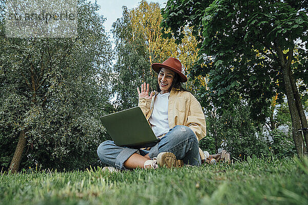 Lächelnde Frau spricht im Park per Videoanruf über Laptop