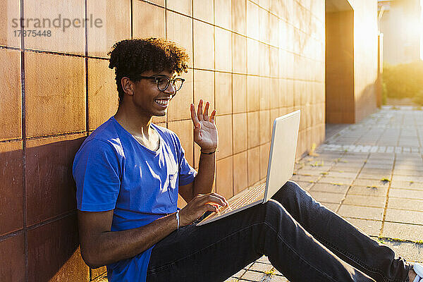 Lächelnder junger Mann  der bei Sonnenuntergang einen Videoanruf über seinen Laptop tätigt
