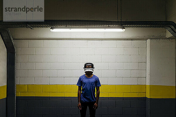 Young man wearing astronaut helmet standing in front of wall at underground walkway