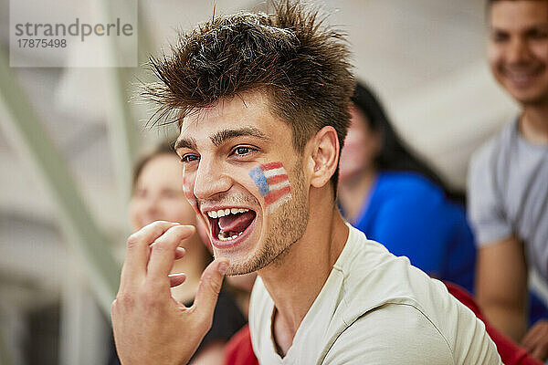 Aufgeregter Mann mit amerikanischer Flagge im Gesicht schreiend im Stadion