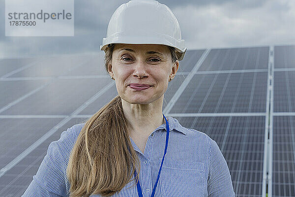 Selbstbewusster Ingenieur mit Helm steht vor Sonnenkollektoren