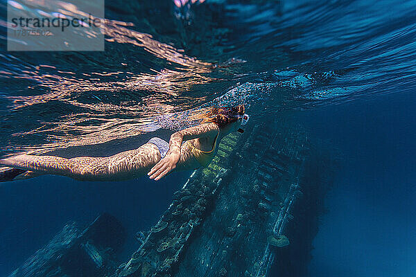 Frau schwimmt in der Nähe eines Schiffswracks im Meer