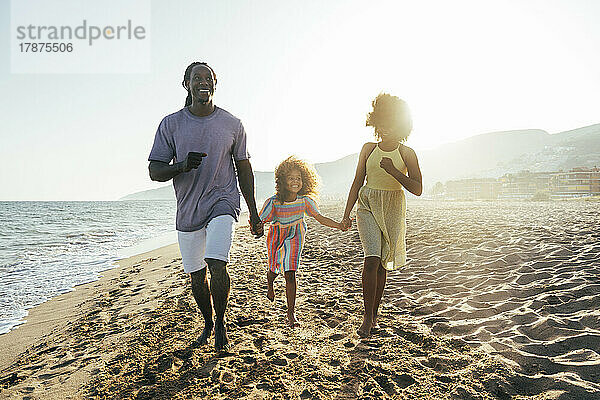 Glückliches Mädchen hält Vater und Schwester an den Händen und läuft am Strand