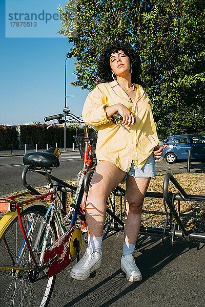 Selbstbewusste Frau mit Fahrrad am Parkplatz an einem sonnigen Tag