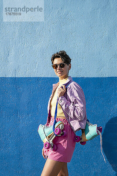 Frau mit Sonnenbrille und Rollschuhen an der blauen Wand