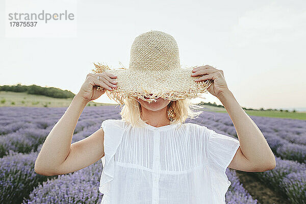 Frau verdeckt Gesicht mit Hut im Lavendelfeld