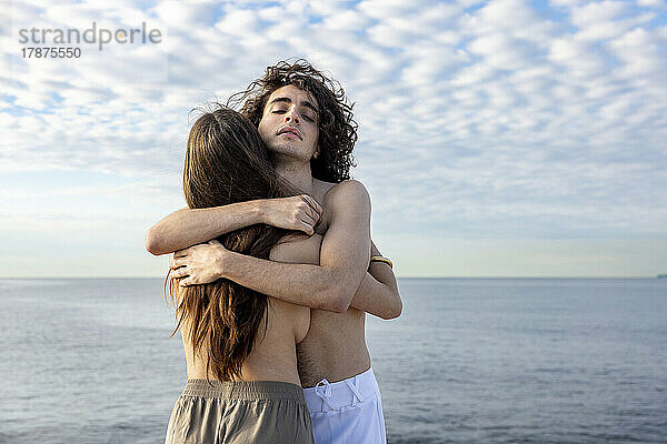 Junge  oben ohne Freundin und Freund umarmen sich vor dem Meer