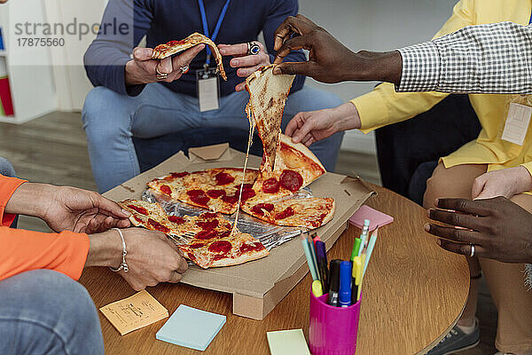 Hände von Geschäftskollegen  die Pizzastücke im Büro halten