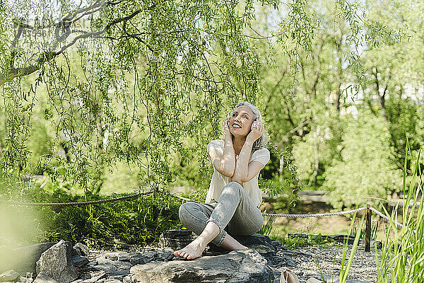 Glückliche Frau  die im Park Musik über Kopfhörer hört