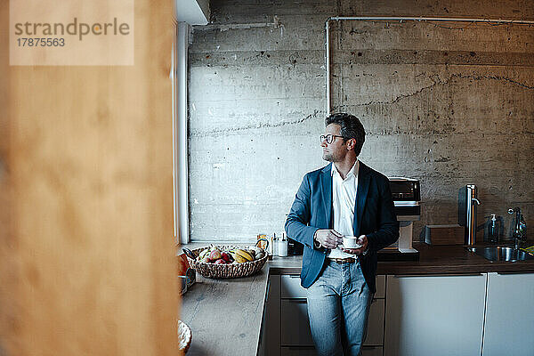 Mature businessman with coffee cup standing in office cafeteria