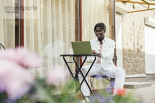 Lächelnder Freiberufler mit Laptop sitzt im Straßencafé