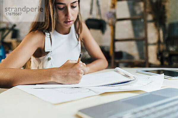 Modedesigner zeichnet am Schreibtisch auf Papier