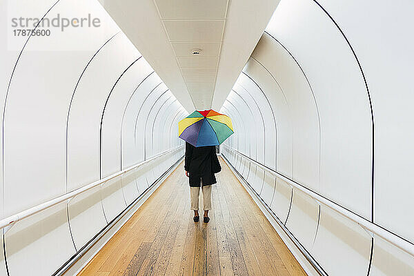 Junge Frau mit Regenschirm steht auf Gehweg