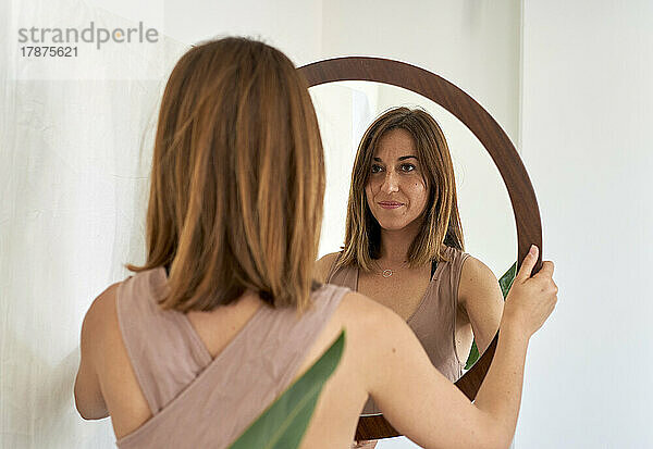 Lächelnde Frau  die zu Hause in den Spiegel schaut