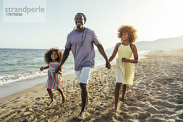 Glücklicher Mann hält die Hände seiner Tochter beim Laufen am Strand