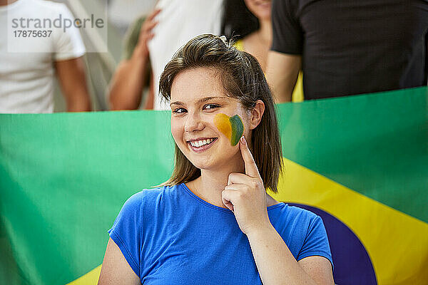 Lächelnde Frau zeigt Brasilien-Flagge auf Gesicht gemalt