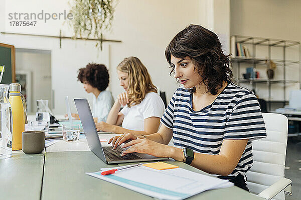 Junge Geschäftsfrau benutzt Laptop auf Tisch im Büro