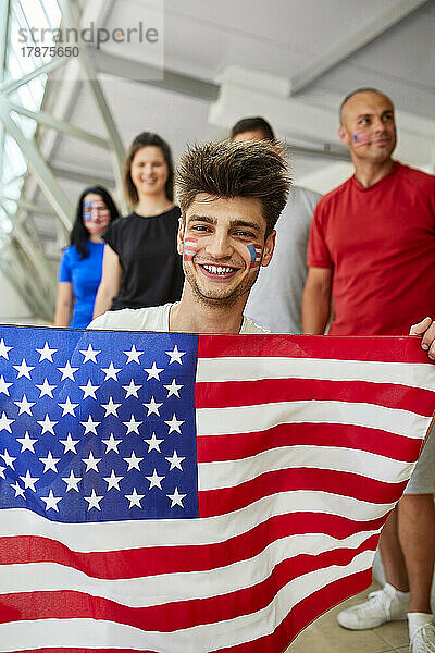 Lächelnder junger Mann mit amerikanischer Flagge bei Sportveranstaltung im Stadion