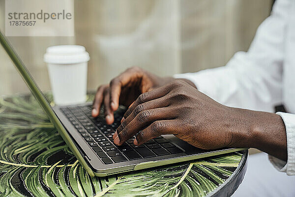Hände eines Freiberuflers  der im Straßencafé am Laptop tippt