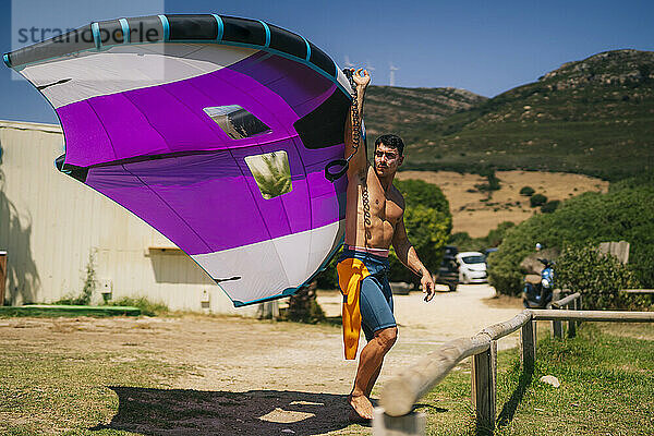 Junger Mann ohne Hemd hält an einem sonnigen Tag ein Tragflügelboot am Strand