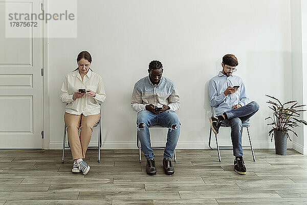 Menschen  die Smartphones benutzen  sitzen auf Stühlen vor der Wand