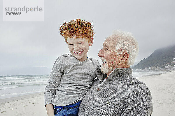Glücklicher Großvater  der seinen Enkel am Meer trägt