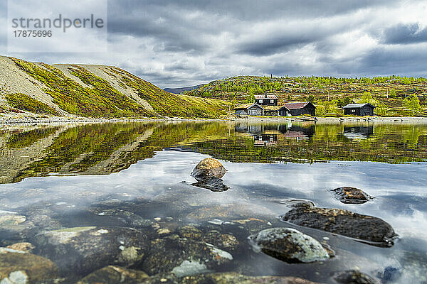 Norwegen  Innlandet  felsiges Seeufer im Jotunheimen-Nationalpark mit abgeschiedenen Hütten im Hintergrund
