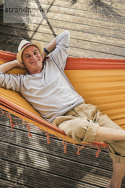 Smiling man with hands behind head lying in hammock
