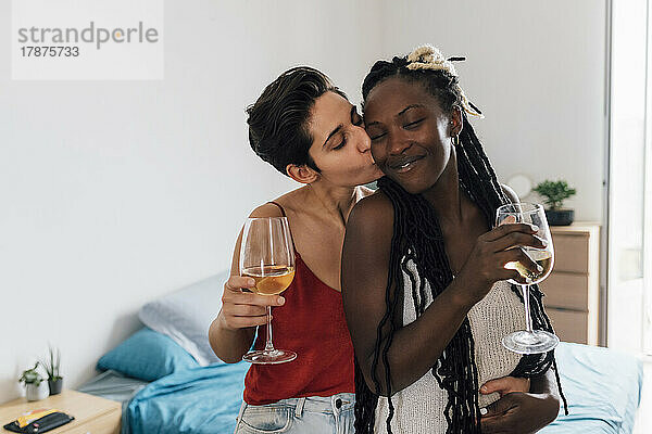 Frau hält Weinglas und küsst Freundin zu Hause