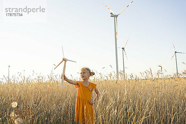 Mädchen hält Windturbinenmodell im Weizenfeld