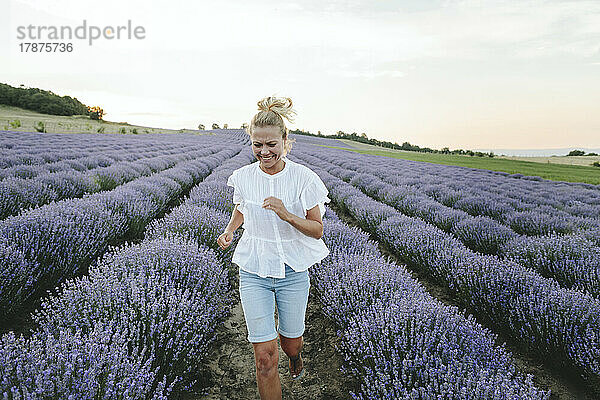 Glückliche Frau  die inmitten von Lavendelpflanzen läuft