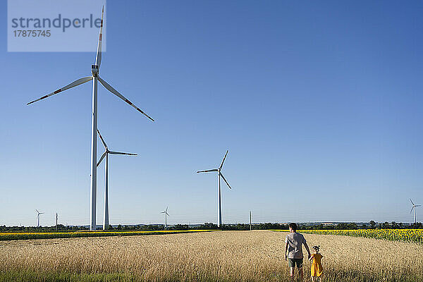 Vater und Tochter stehen neben Windkraftanlagen auf dem Feld